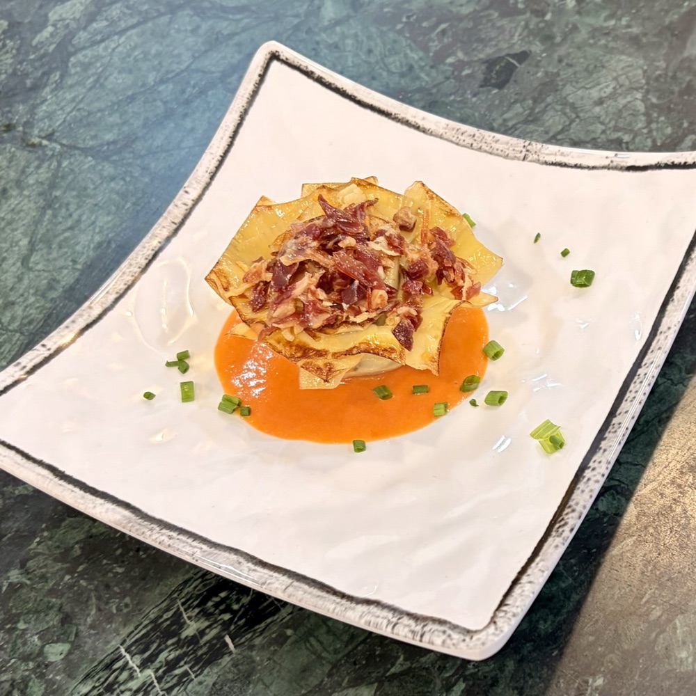Alcachofa confitada y terminada a la plancha sobre una cama de salmorejo, con virutas de jam&oacute;n ib&eacute;rico, ajo macerado y cebollino